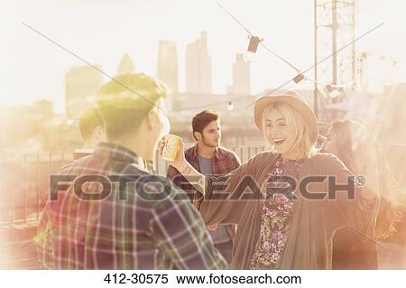 Stock Photography - Enthusiastic young adults enjoying rooftop party. Fotosearch