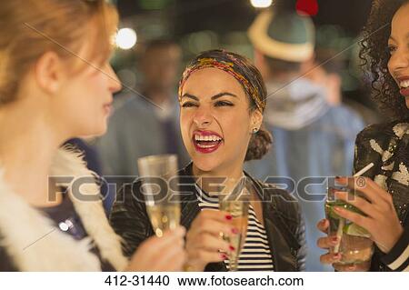 Stock Image - Enthusiastic young women drinking champagne and laughing at party. Fotosearch