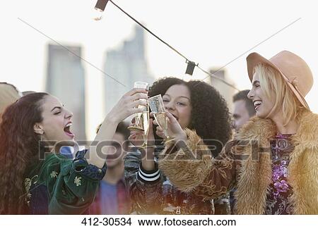 Picture - Enthusiastic young women toasting champagne glasses at rooftop party. Fotosearch