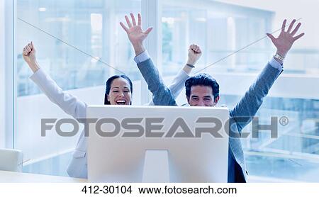Picture - Exuberant businessman and businesswoman cheering with arms raised at computer in office. Fotosearch