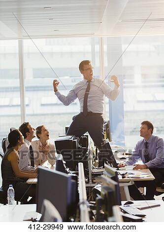 Stock Photo - Exuberant businessman celebrating on top of desks in office. Fotosearch