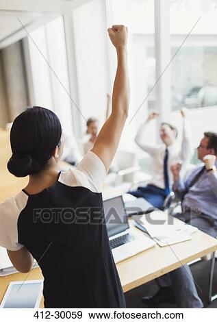 Exuberant businesswoman gesturing with fist and celebrating with colleagues in conference room View Large Photo Image Stock Photo - Exuberant businesswoman gesturing with fist and celebrating with colleagues in conference room. Fotosearch