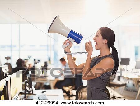Picture - Exuberant businesswoman using megaphone in office. Fotosearch