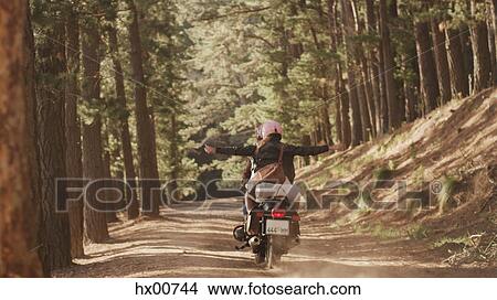 Picture - Exuberant young woman riding motorcycle on dirt road in woods. Fotosearch
