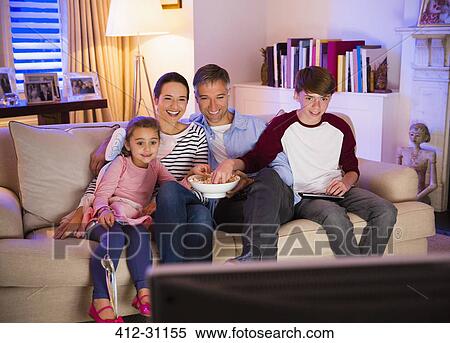 Stock Photography - Family eating popcorn and watching TV in living room. Fotosearch