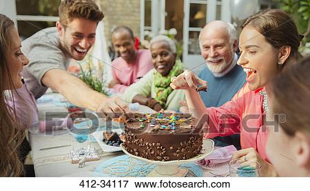 Stock Photo - Family reaching for candy on chocolate birthday cake at patio table. Fotosearch