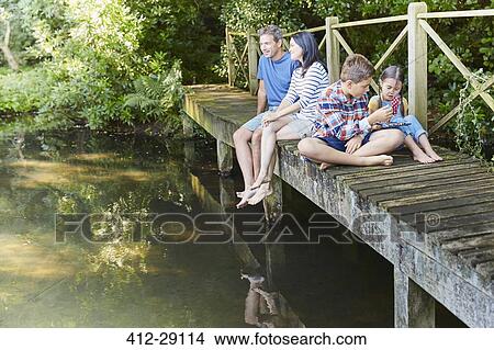 Picture - Family relaxing on footbridge over pond. Fotosearch