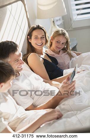 Family relaxing with digital tablet in bed View Large Photo Image Stock Photography - Family relaxing with digital tablet in bed. Fotosearch
