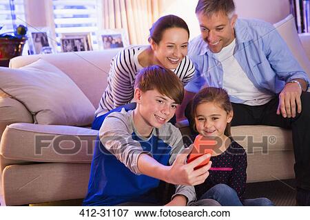 Stock Photo - Family taking selfie with camera phone in living room. Fotosearch