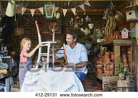 Stock Image - Father and daughter painting chair in workshop. Fotosearch