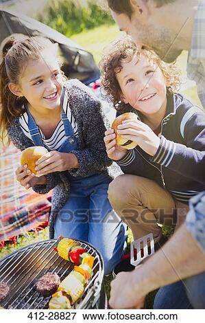 Stock Photo - Father and kids eating hamburgers at barbecue grill. Fotosearch