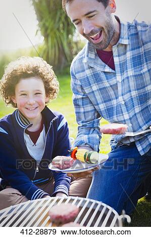 Father and son barbecuing hamburgers and vegetable skewers at grill View Large Photo Image Stock Photo - Father and son barbecuing hamburgers and vegetable skewers at grill. Fotosearch