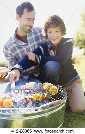 Stock Photograph - Father and son barbecuing hamburgers and vegetable skewers. Fotosearch