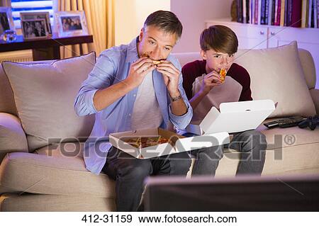 Father and son eating pizza and watching TV in living room View Large Photo Image Stock Photo - Father and son eating pizza and watching TV in living room. Fotosearch