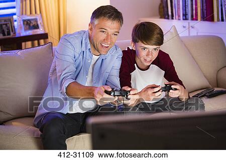 Stock Photo - Father and son playing video game in living room. Fotosearch