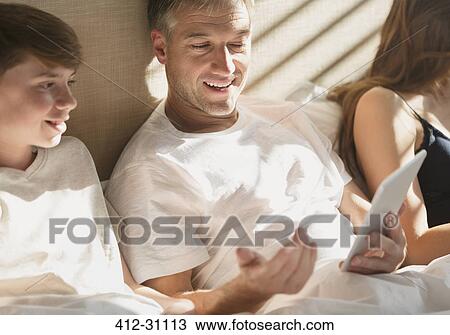 Stock Image - Father and son using digital tablet in bed. Fotosearch