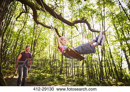 Father pushing daughter on rope swing in forest View Large Photo Image Stock Image - Father pushing daughter on rope swing in forest. Fotosearch