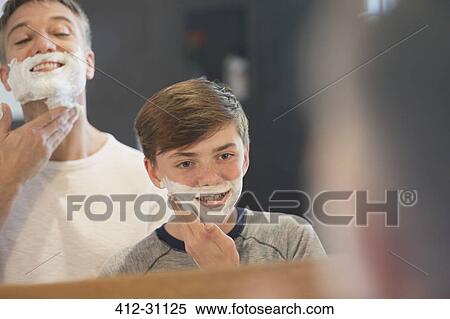 Stock Photography - Father watching son pretending to shave face in bathroom mirror. Fotosearch