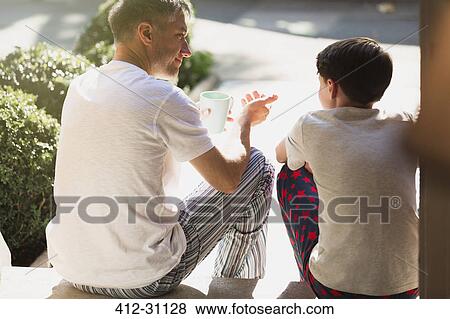 Stock Photo - Father with coffee talking to son on front stoop. Fotosearch