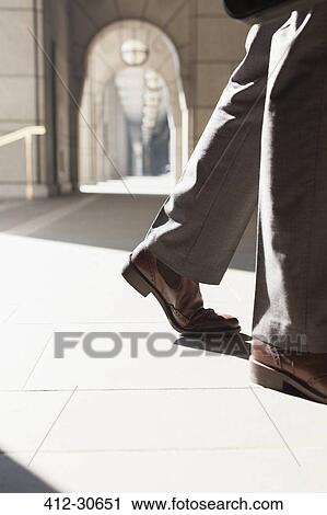 Stock Image - Feet of corporate businessman walking in sunny cloister. Fotosearch