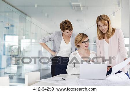 Stock Photo - Female architects at laptop reviewing blueprints in conference room meeting. Fotosearch