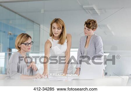 Stock Photography - Female architects discussing blueprint at laptop in conference room meeting. Fotosearch