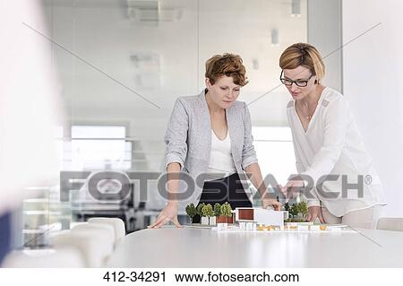 Stock Image - Female architects discussing model in conference room. Fotosearch