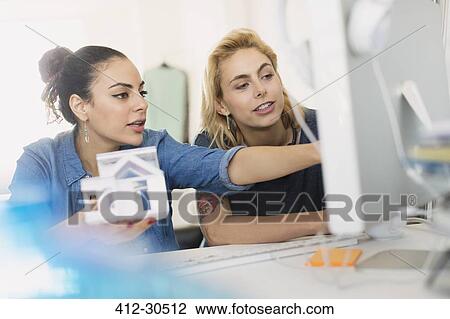 Stock Image - Female architects holding house model at computer in office. Fotosearch