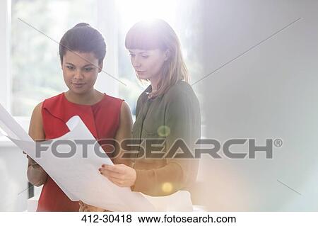 Stock Photo - Female architects reviewing blueprints in office. Fotosearch
