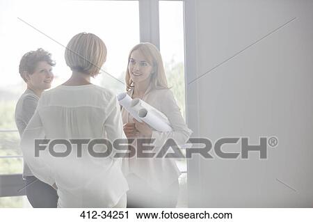 Female architects with blueprints talking in office View Large Photo Image Stock Image - Female architects with blueprints talking in office. Fotosearch