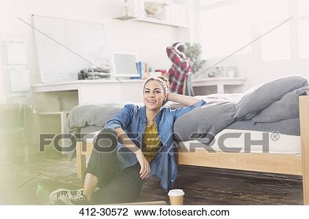 Stock Image - Female college student relaxing on bedroom floor. Fotosearch