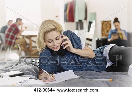 Female college student studying and talking on cell phone on bed View Large Photo Image Picture - Female college student studying and talking on cell phone on bed. Fotosearch