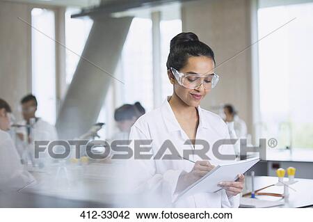 Stock Image - Female college student taking notes in science laboratory classroom. Fotosearch