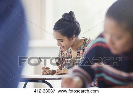 Stock Photo - Female college student taking test at desk in classroom. Fotosearch
