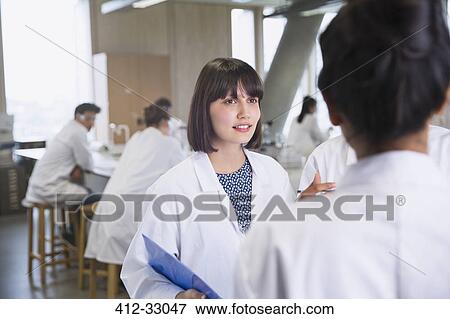 Stock Photo - Female college students in lab coats talking in science laboratory classroom. Fotosearch