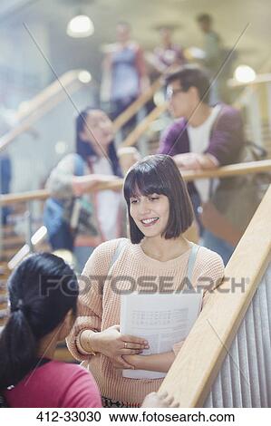 Stock Image - Female college students talking in stairway. Fotosearch