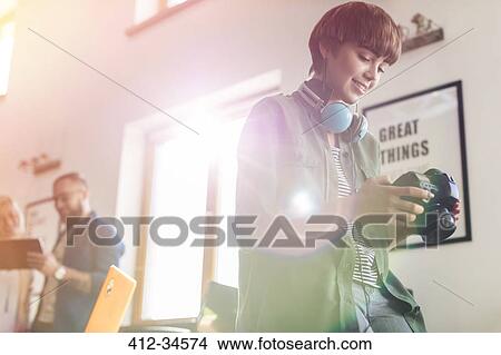 Picture - Female design professional with headphones using SLR camera in office. Fotosearch