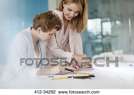 Stock Image - Female designers reviewing sketch drawings in conference room meeting. Fotosearch