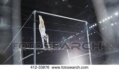 Stock Photograph - Female gymnast performing on uneven bars in arena. Fotosearch
