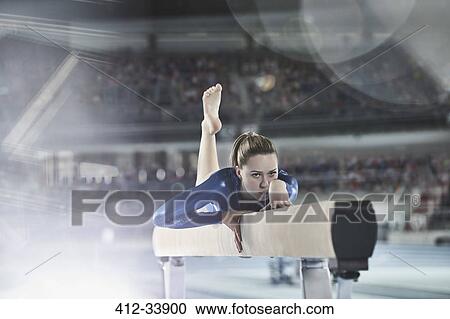 Stock Image - Female gymnast practicing on balance beam in arena. Fotosearch