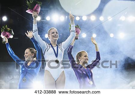 Female gymnasts celebrating victory waving on winners podium View Large Photo Image Stock Photo - Female gymnasts celebrating victory waving on winners podium. Fotosearch