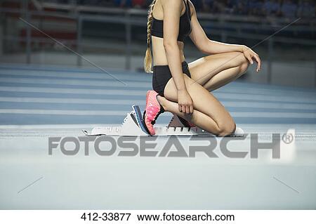 Female runner kneeling at starting block on sports track View Large Photo Image Stock Photo - Female runner kneeling at starting block on sports track. Fotosearch