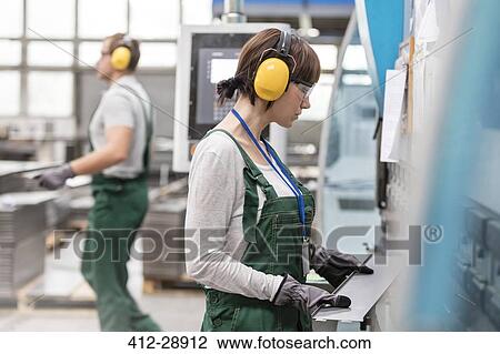 Female worker with ear protectors holding metal part in factory View Large Photo Image Stock Image - Female worker with ear protectors holding metal part in factory. Fotosearch