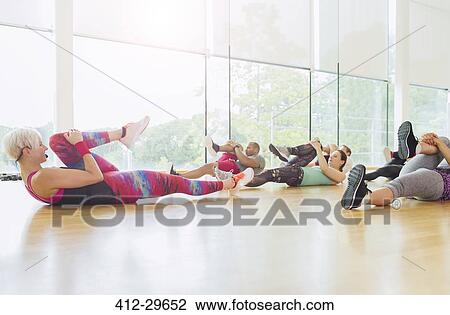 Stock Image - Fitness instructor guiding exercise class stretching legs. Fotosearch