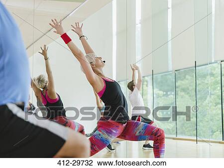 Stock Image - Fitness instructor leading aerobics class in high lunge. Fotosearch