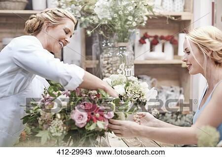Stock Image - Florist arranging bouquet for customer in flower shop. Fotosearch