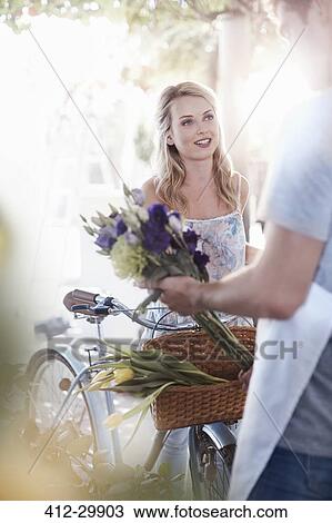 Florist placing flowers in basket on womans bicycle View Large Photo Image Stock Image - Florist placing flowers in basket on womans bicycle. Fotosearch