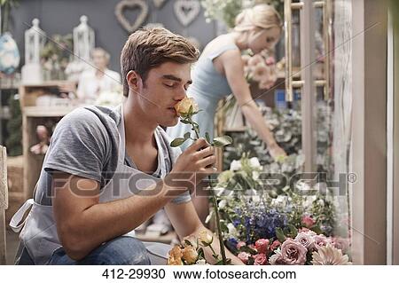 Stock Image - Florist smelling rose in flower shop. Fotosearch