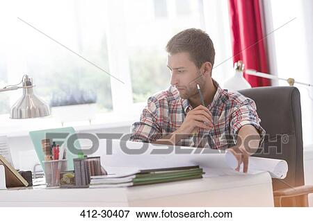 Focused architect with blueprints working at laptop in office View Large Photo Image Stock Photo - Focused architect with blueprints working at laptop in office. Fotosearch