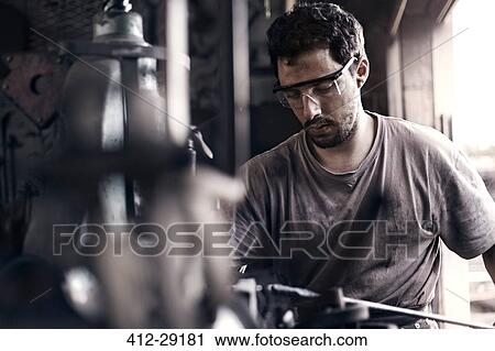 Stock Image - Focused blacksmith shaping iron in forge. Fotosearch